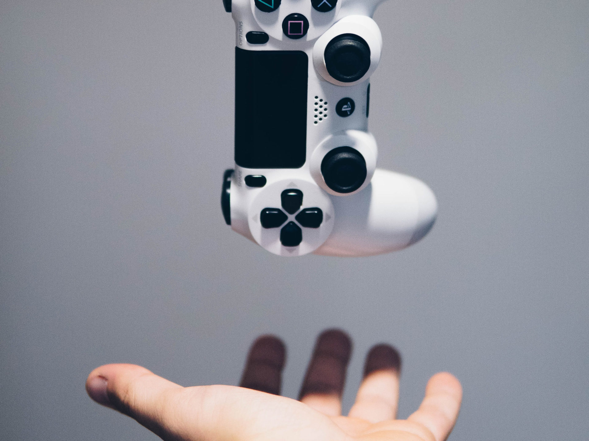 A hand outstretched ready to catch a Playstation 4 controller that is falling back into the frame