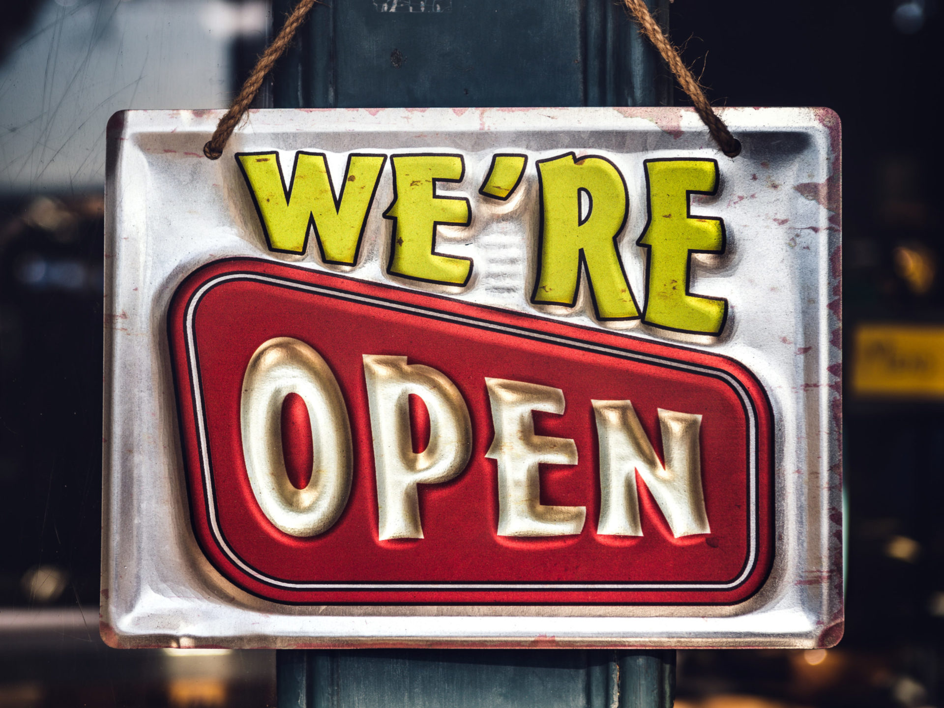 A metal sign with the words "we're open" we're in yellow and Open surrounded by a red rectangle