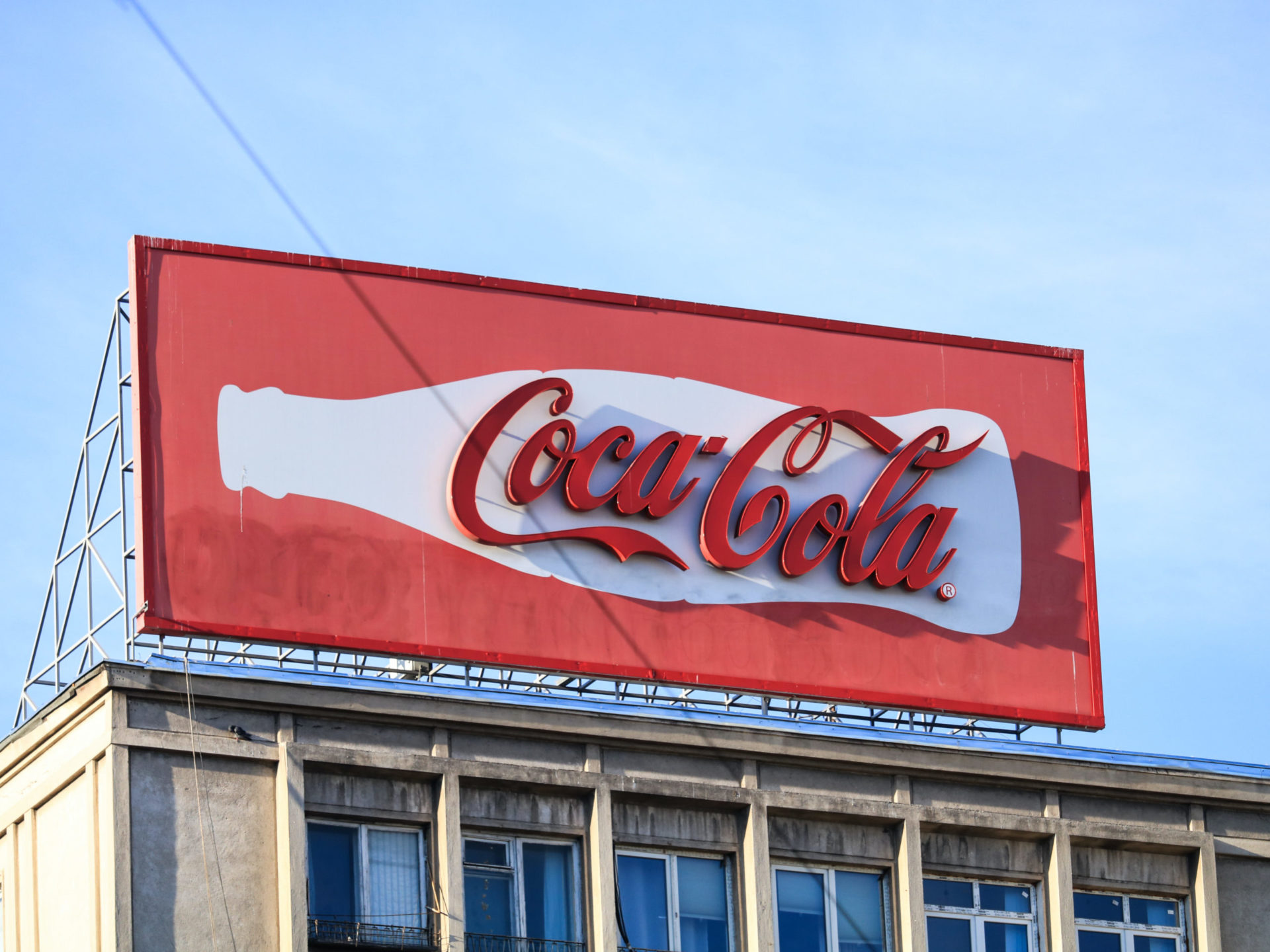 A billboard on top of a building wwith the CocaCola logo protruding out from a white silhouette of a coke bottle