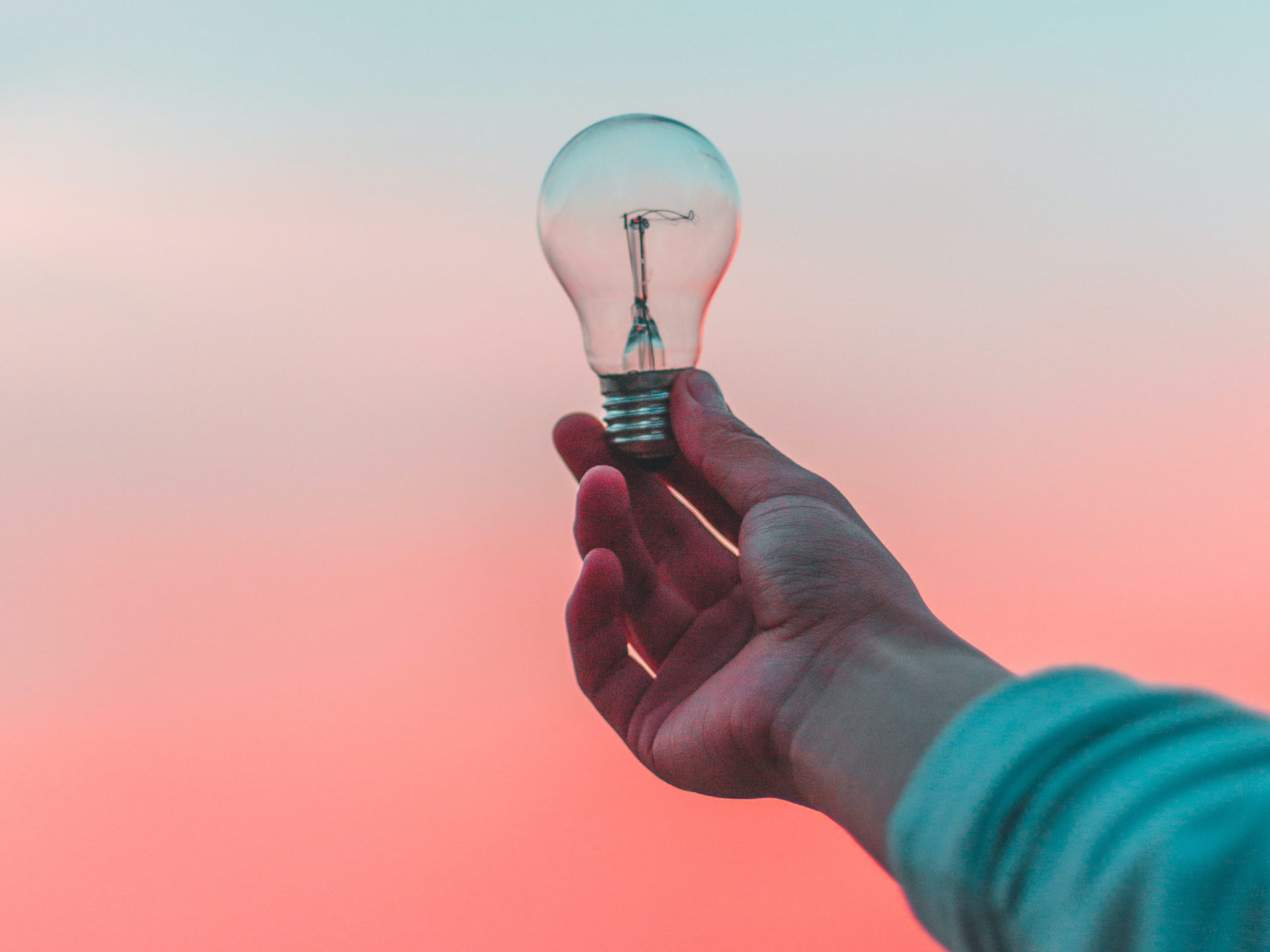 hand holding a lightbulb in front of a bright blue, white, and pink gradient background