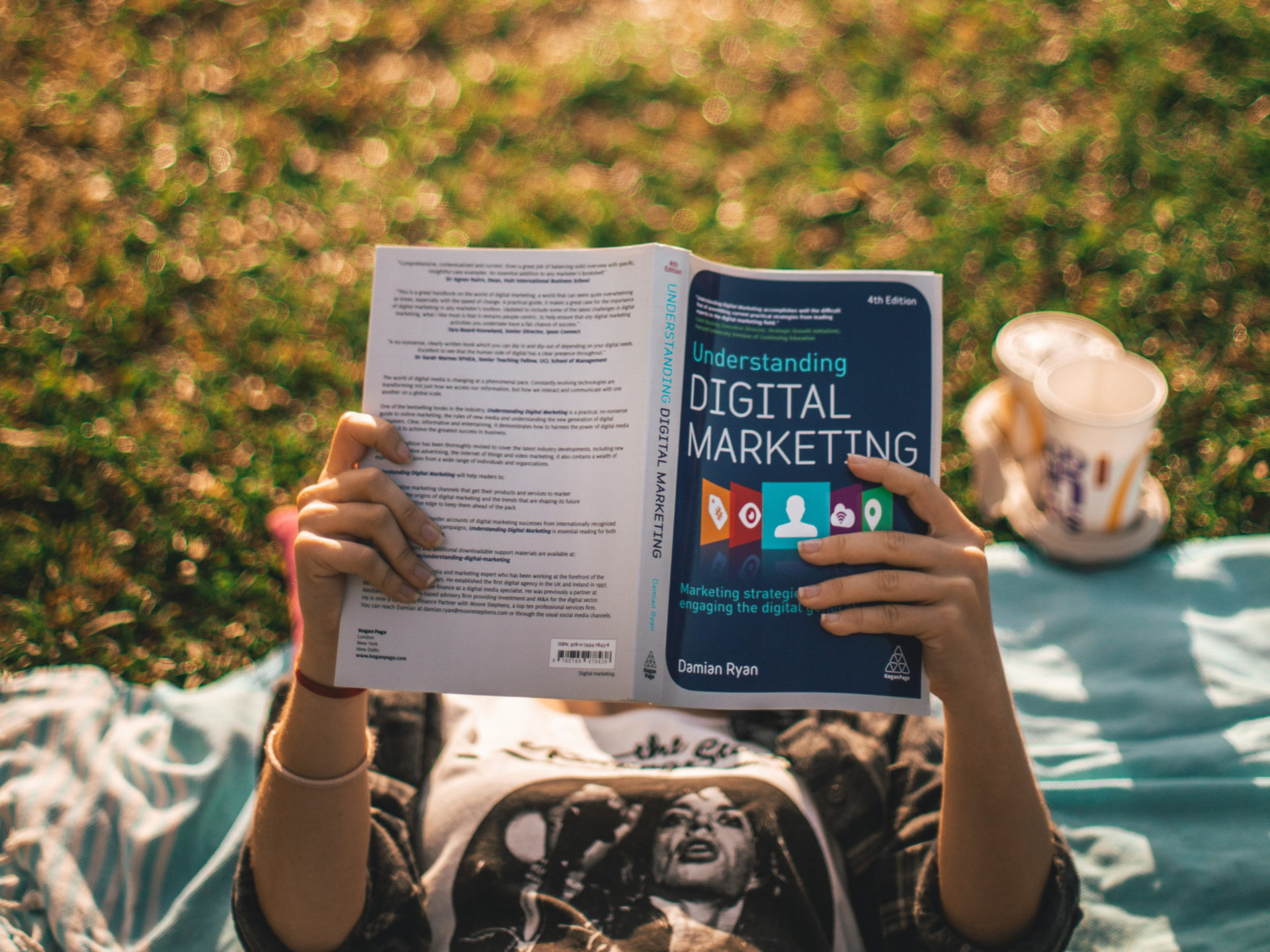 A person laying on a blanket in some grass, reading a book with the title "digital marketing"